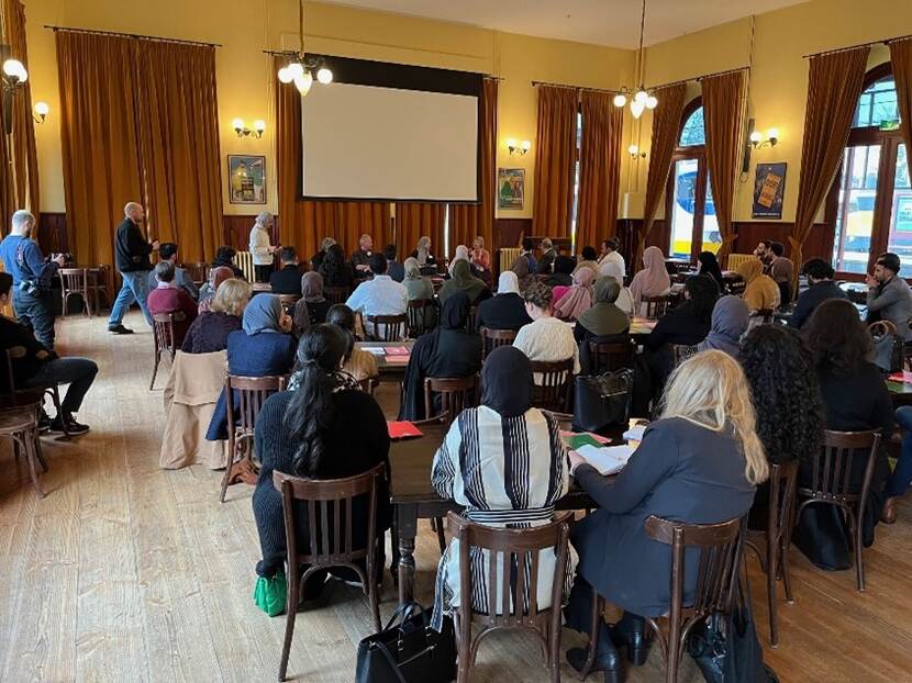 Een zaal gevuld met mensen kijkt richting een panel van sprekers.